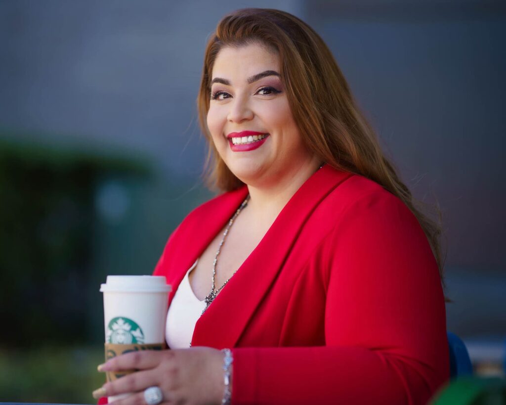 Woman in red jacket and holding a Starbucks cup sitting and posing.