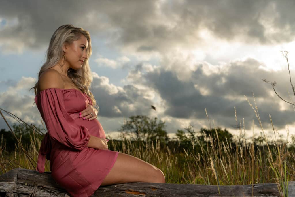 Pregnant woman sitting on a log in a field in the morning.