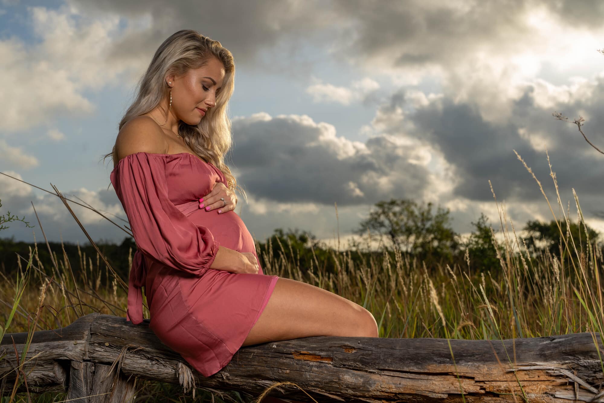 Pregnant woman sitting on a log in a field.