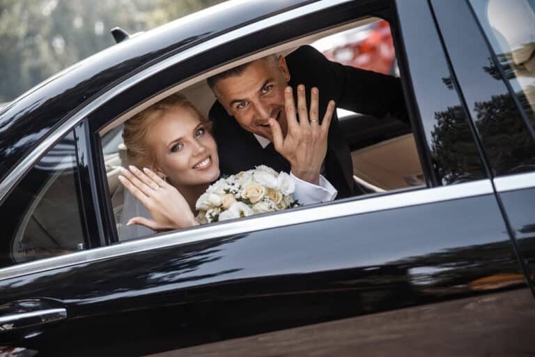 The newlyweds are showing their rings at the camera while sitting in the car.