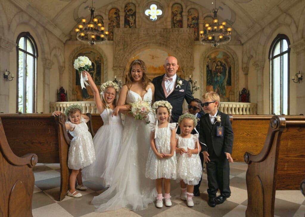 Bride, groom, ring-bearers and flower girls posing in a chapel.