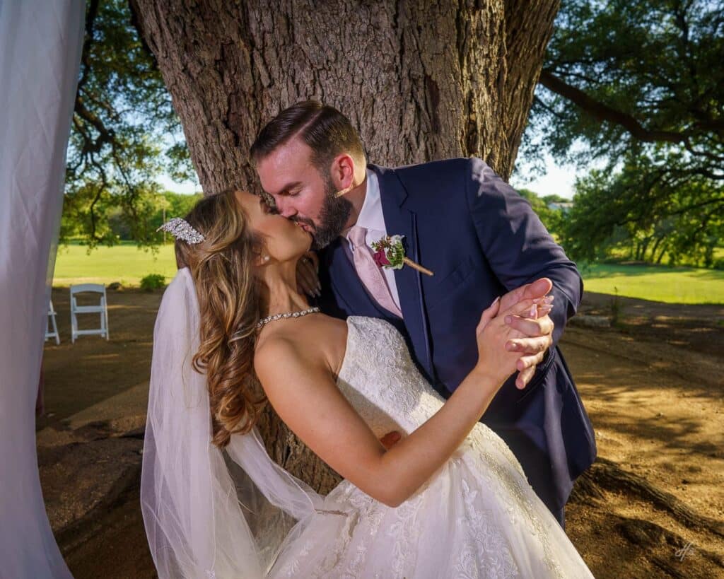 Newlyweds kissing under a tree.