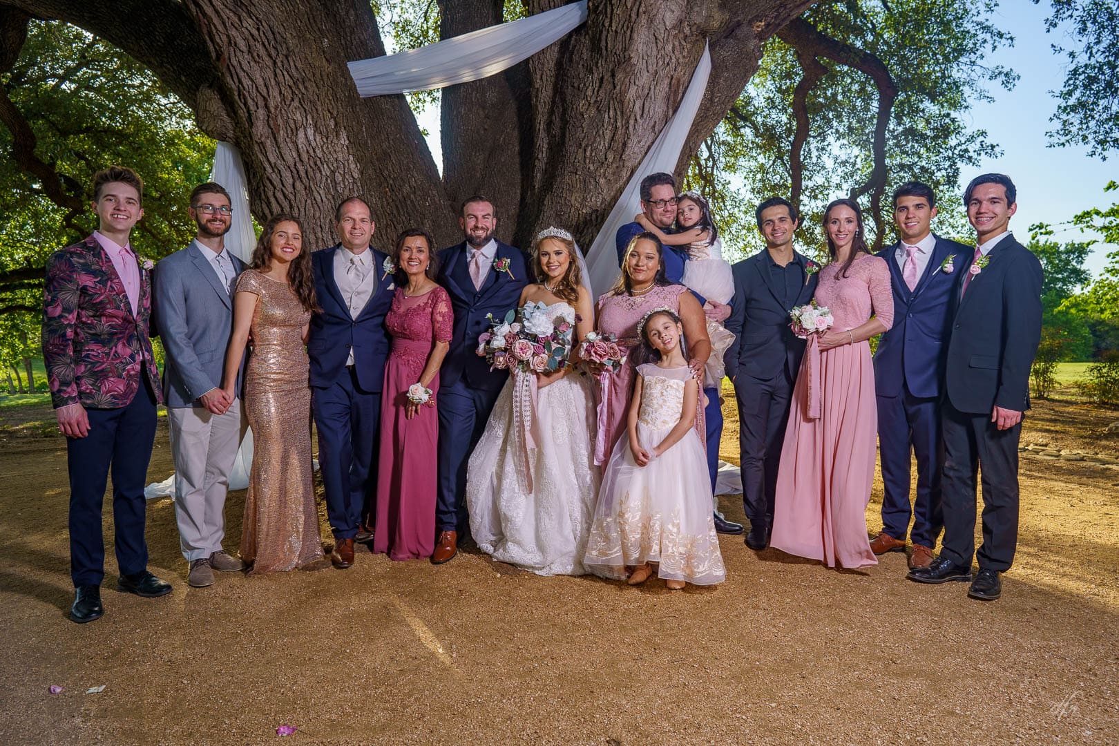 Newlyweds pose with family under a tree.