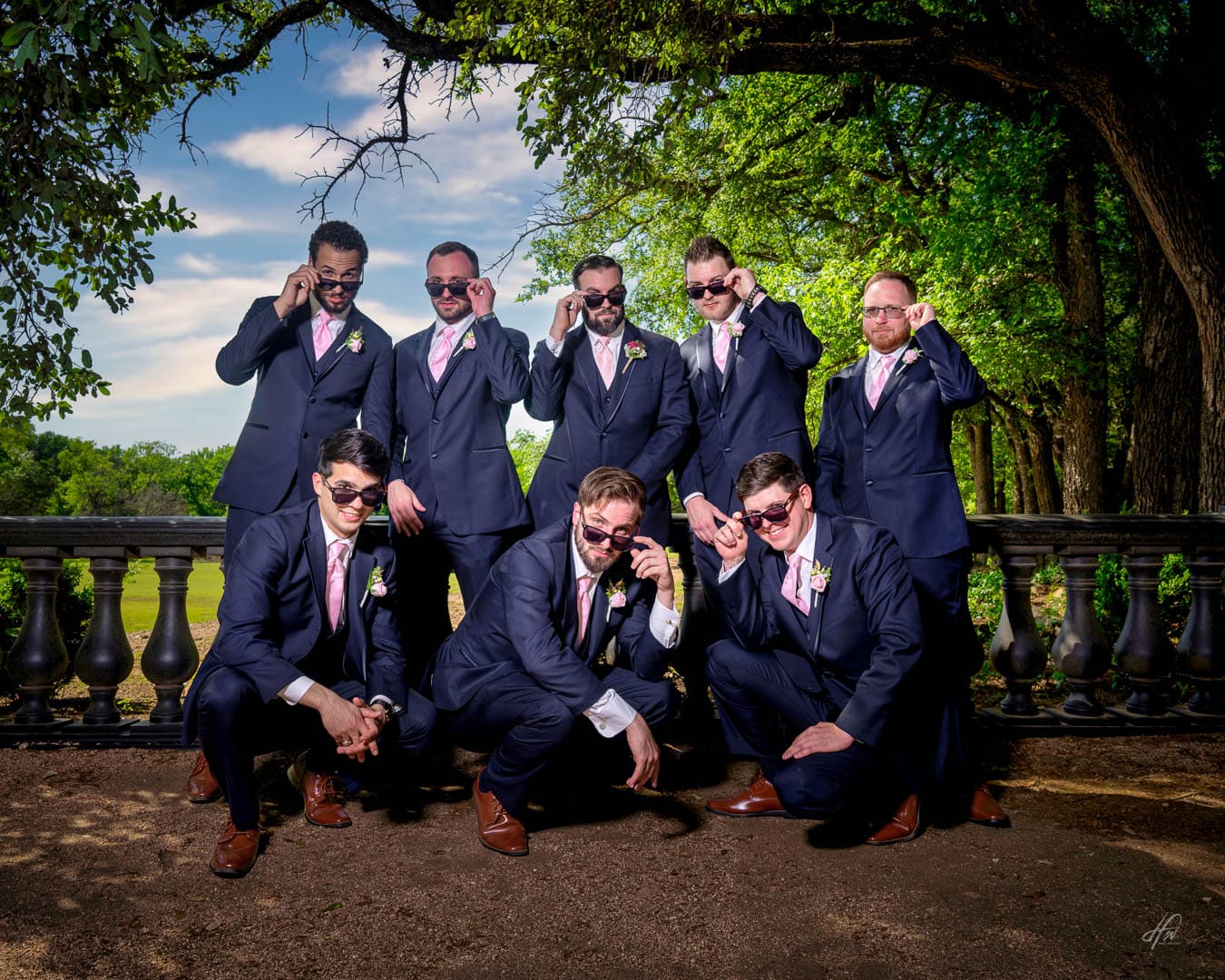 Groom and 7 groomsmen in blue suits and pink ties looking over the tops of their sunglasses.
