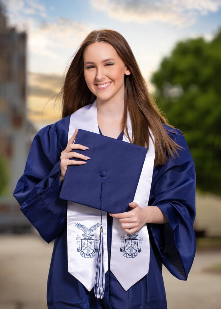 Greaduation photo of a high school grad in a blue gown holding her cap.